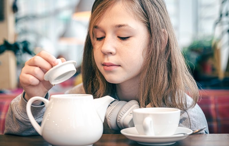 Portrait of a little girl in a cafe with a teapot and a cup.